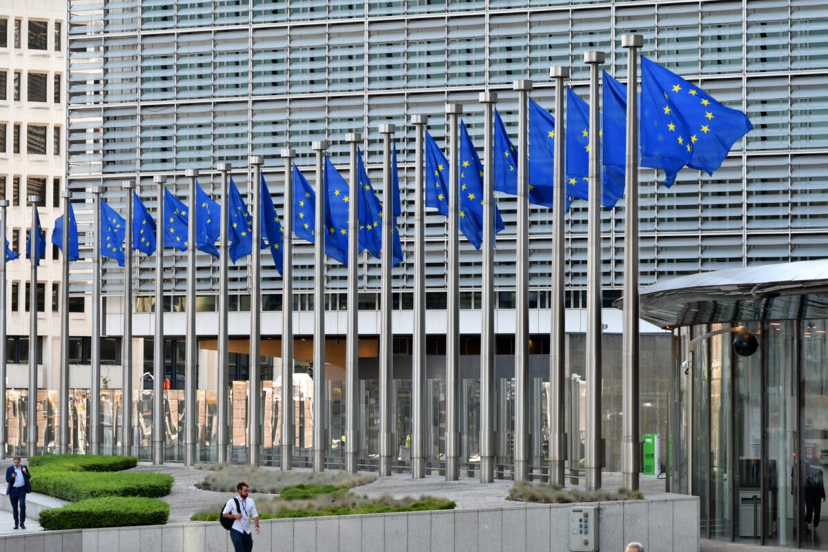 Rad med EU-flagg blafrer foran en moderne bygningsfasade med folk som går i nærheten.