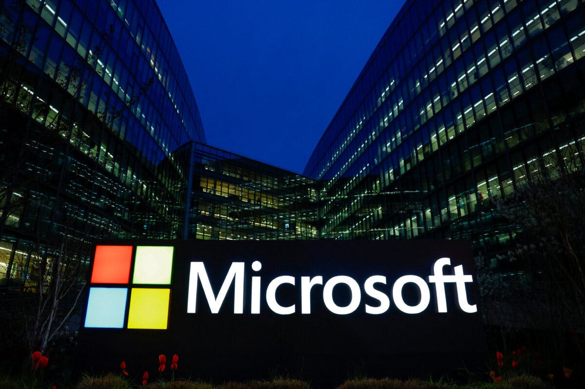 En stor opplyst Microsoft-logo foran en moderne kontorbygning i glass om natten.