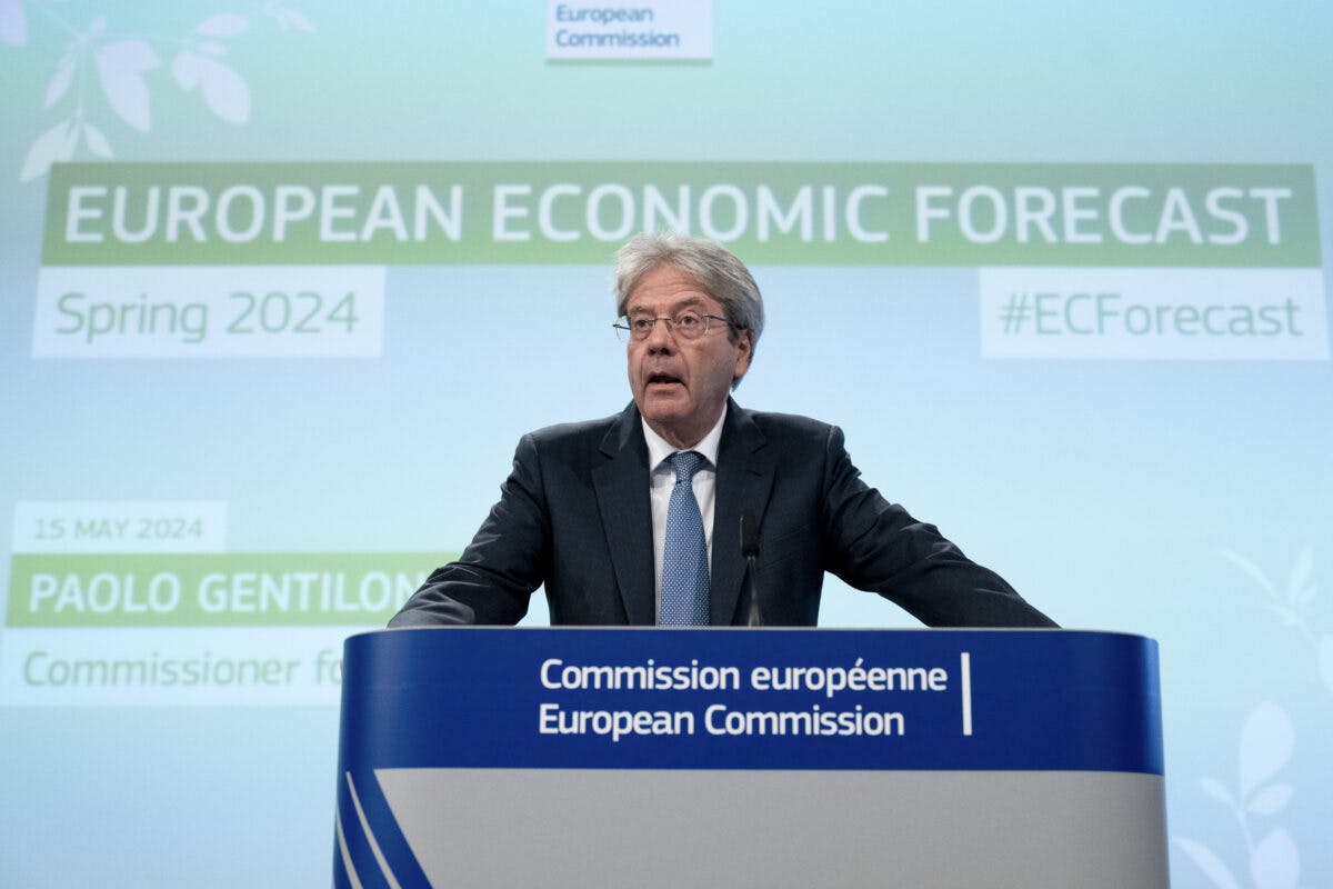 En mann står ved et podium merket "European Commission" under presentasjonen av den europeiske økonomiske vårprognosen 2024. Tekst på skjermen inkluderer "European Economic Forecast" og "Paolo Gentiloni.