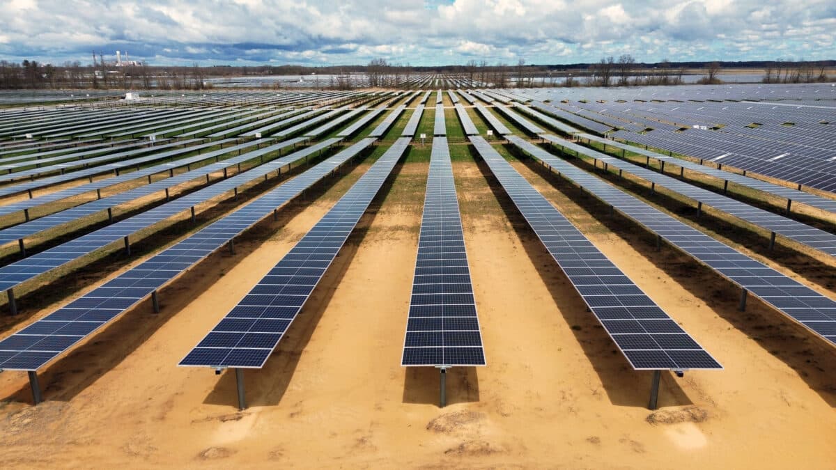 Et stort felt med solcellepaneler er arrangert i parallelle rader under en delvis overskyet himmel.