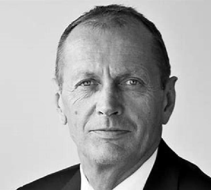 Svart-hvitt portrett av en middelaldrende mann i dress, som ser direkte på kameraet mot en vanlig bakgrunn.