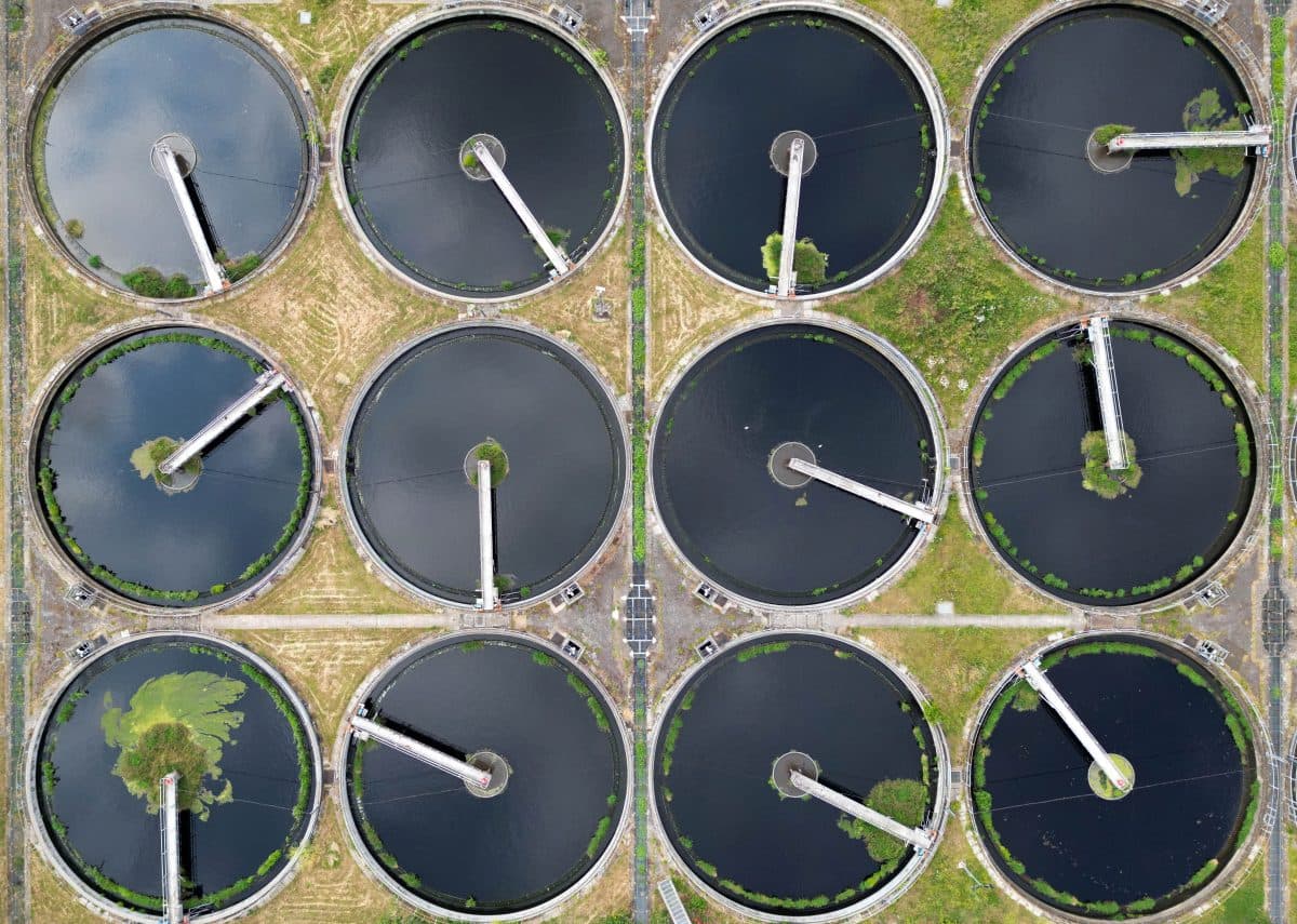Flyfoto av tolv sirkulære vannbehandlingstanker plassert i et rutenett, med grøntområder og stier mellom dem.