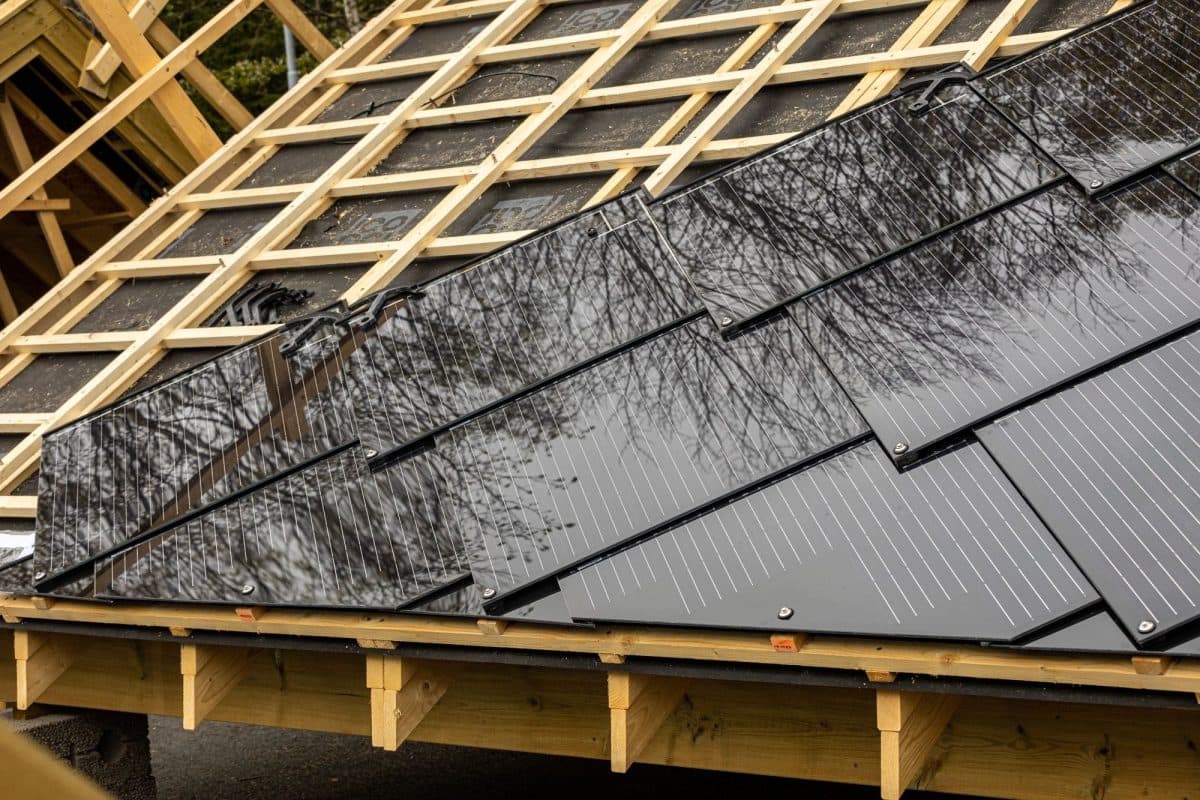 Nærbilde av et tak under konstruksjon med svarte soltakshingel delvis montert ved siden av eksponert treverk.