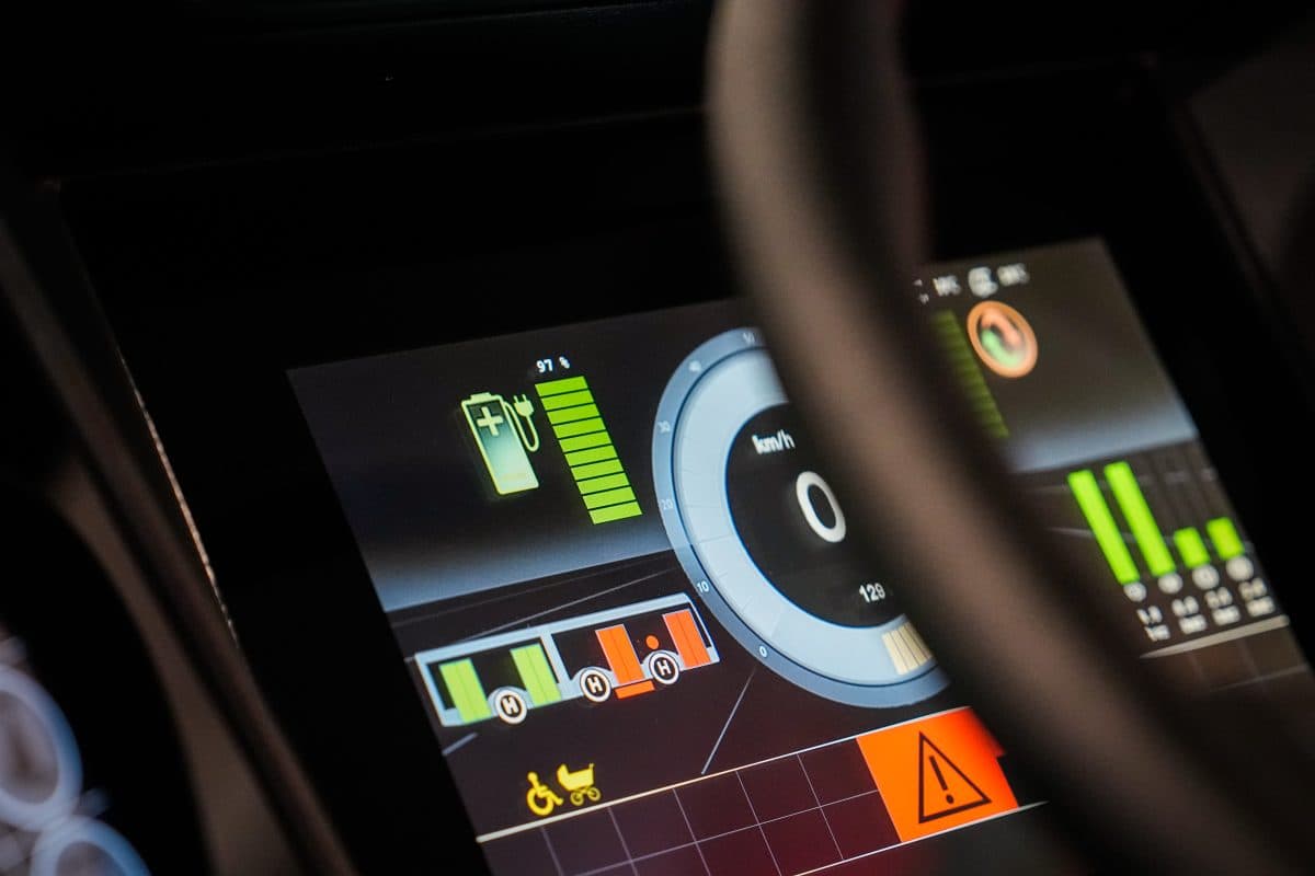 Nærbilde av et digitalt instrumentpanel som viser hastighet, batterinivå og flere indikatorlamper i et elektrisk kjøretøy.