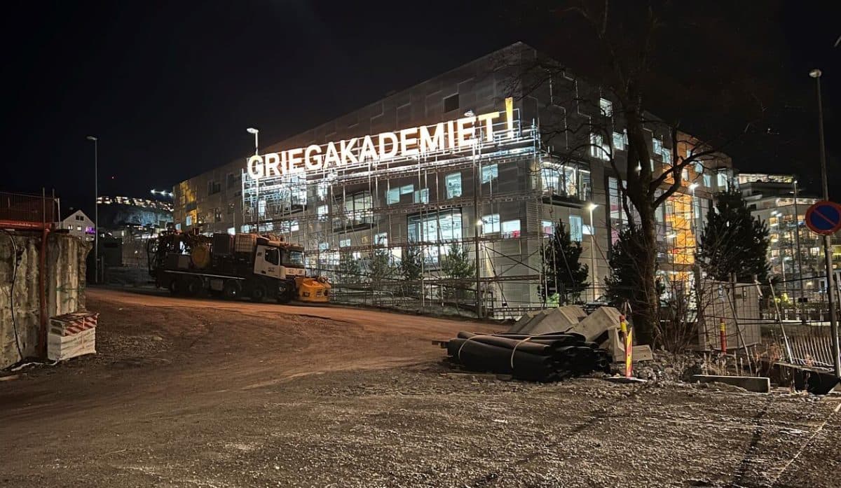 En byggeplass om natten med en bygning i bakgrunnen med lysende bokstaver som viser "GRIEGAKADEMIET".