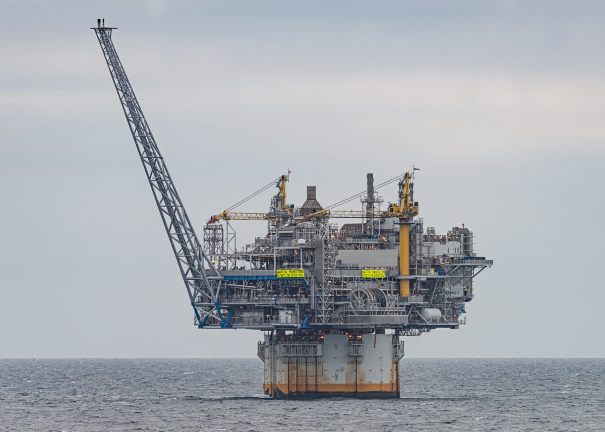Oljeplattformen står ute i havet, med kraner, maskineri og en lang, vinklet bom som strekker seg mot venstre.