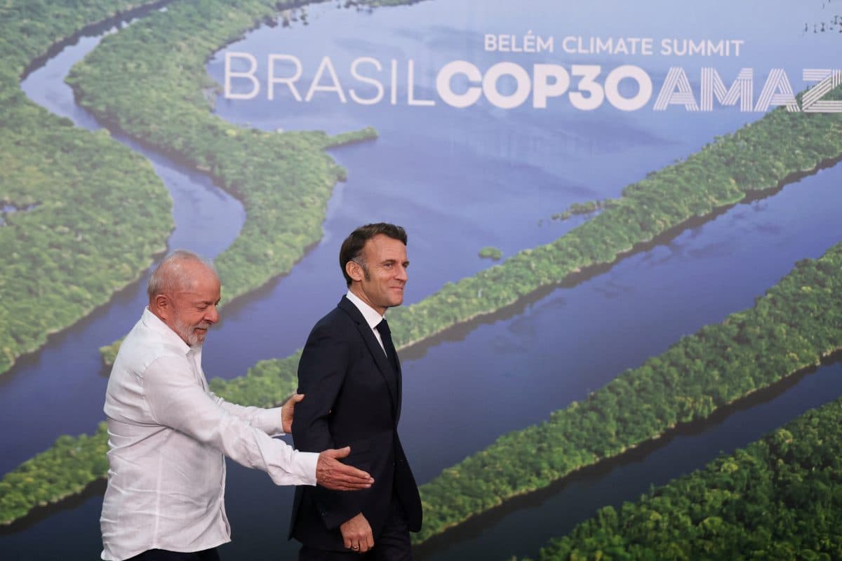 To menn går forbi et bakteppe med et flyfoto av Amazonas-elven og teksten "BRASIL COP30 AMAZÔNIA BELÉM CLIMATE SUMMIT".
