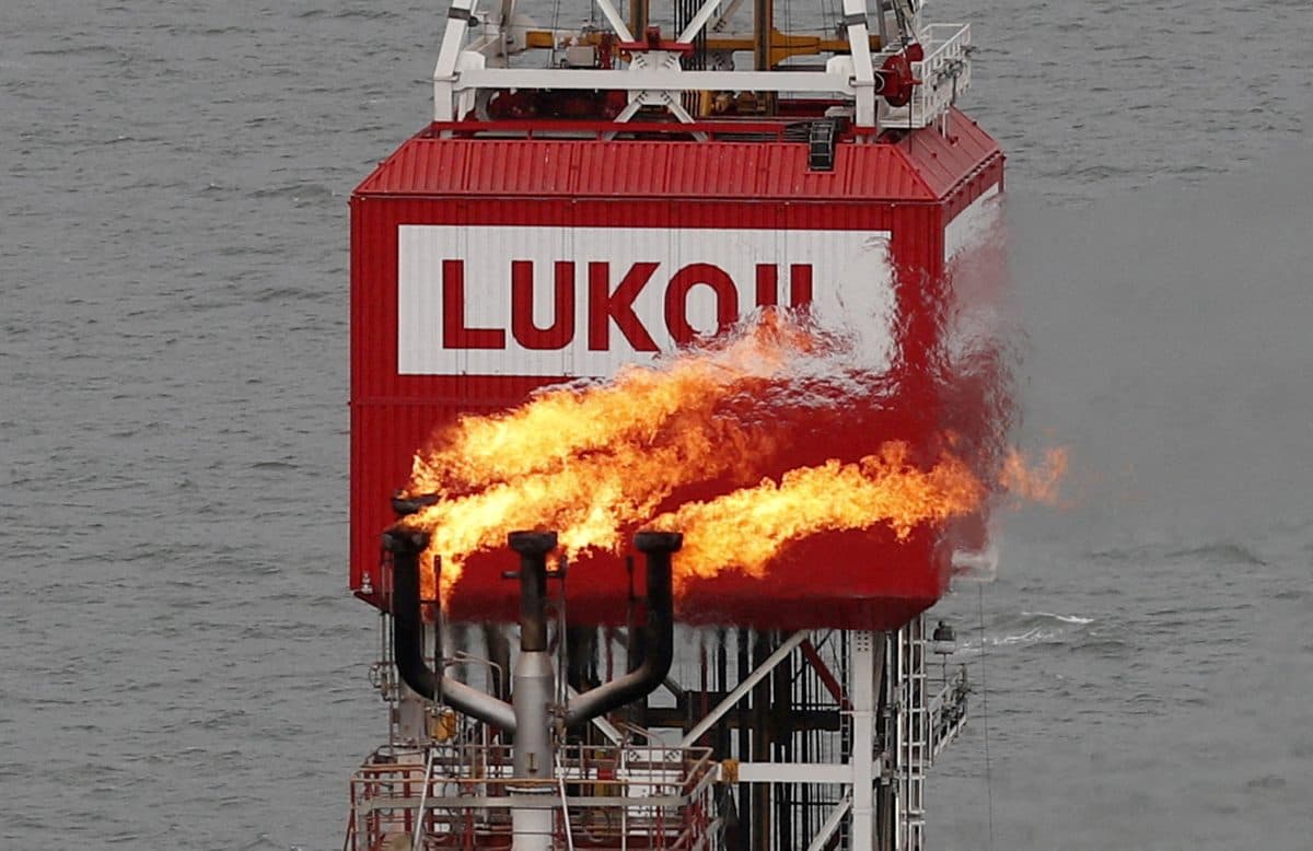 En fakkelstabel brenner av gass på en oljeplattform til havs med en stor rød struktur merket "LUKOIL" mot en bakgrunn av vann.