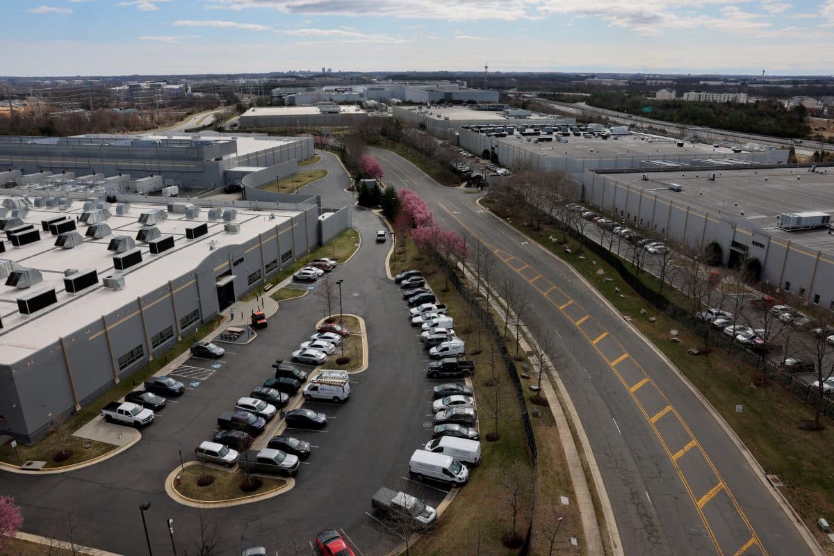 Flyfoto av en stor industripark med flere lagerbygninger, parkeringsplasser fylt med biler og omkringliggende veier kantet av blomstrende trær.
