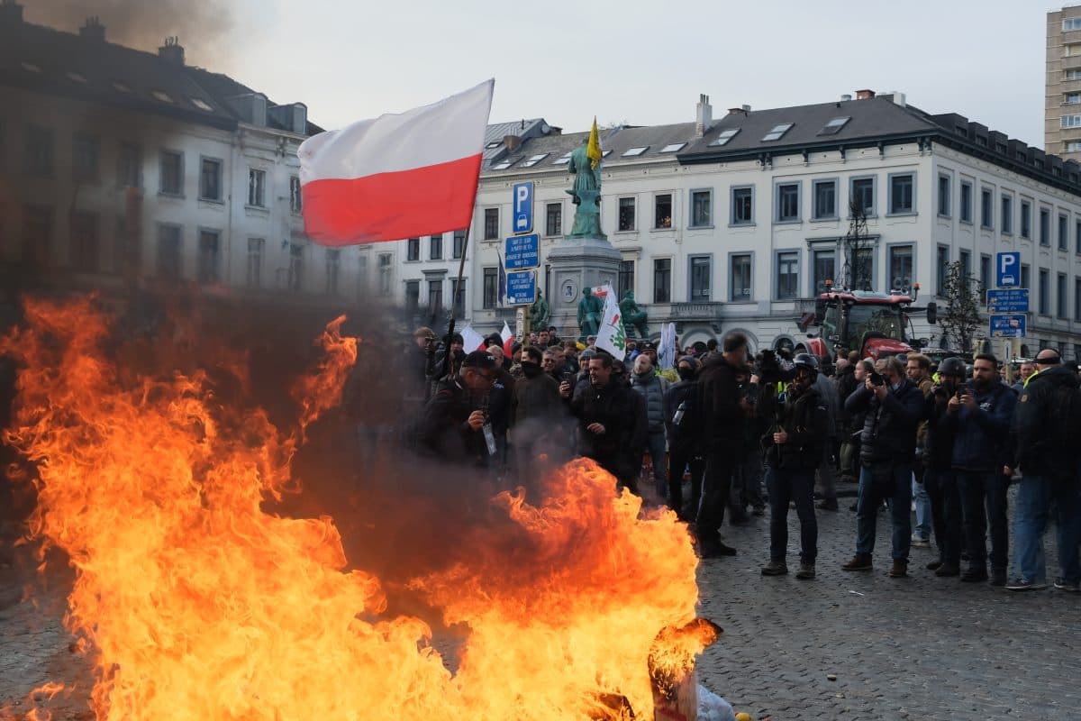 En gruppe demonstranter står bak et stort bål på en brosteinsbelagt gate, mens en person holder et polsk flagg og andre holder skilt.