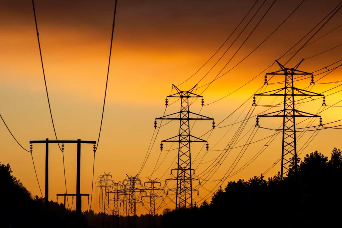 Høyspentledninger og master strekker seg over et landskap i solnedgang, i silhuett mot en oransje og gul himmel.