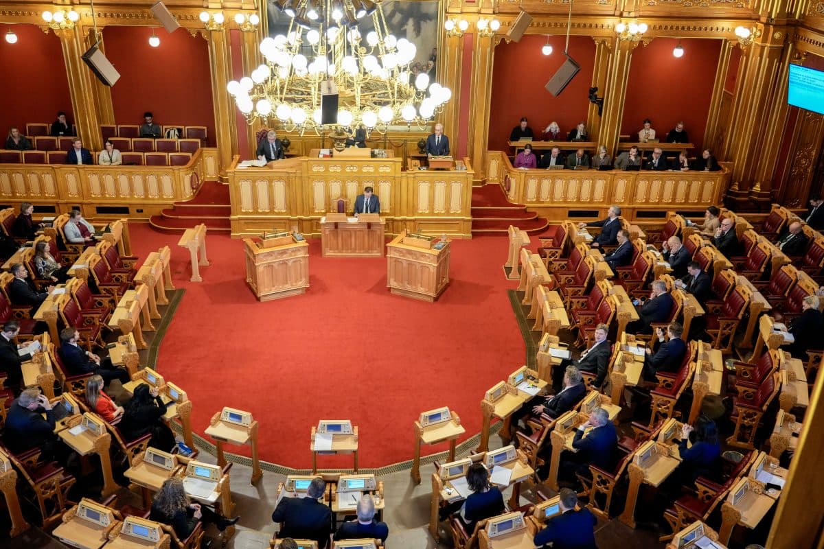 En parlamentssal med politikere som sitter på rekke og rad, en taler på podiet i midten og en utsmykket lysekrone over hodet.