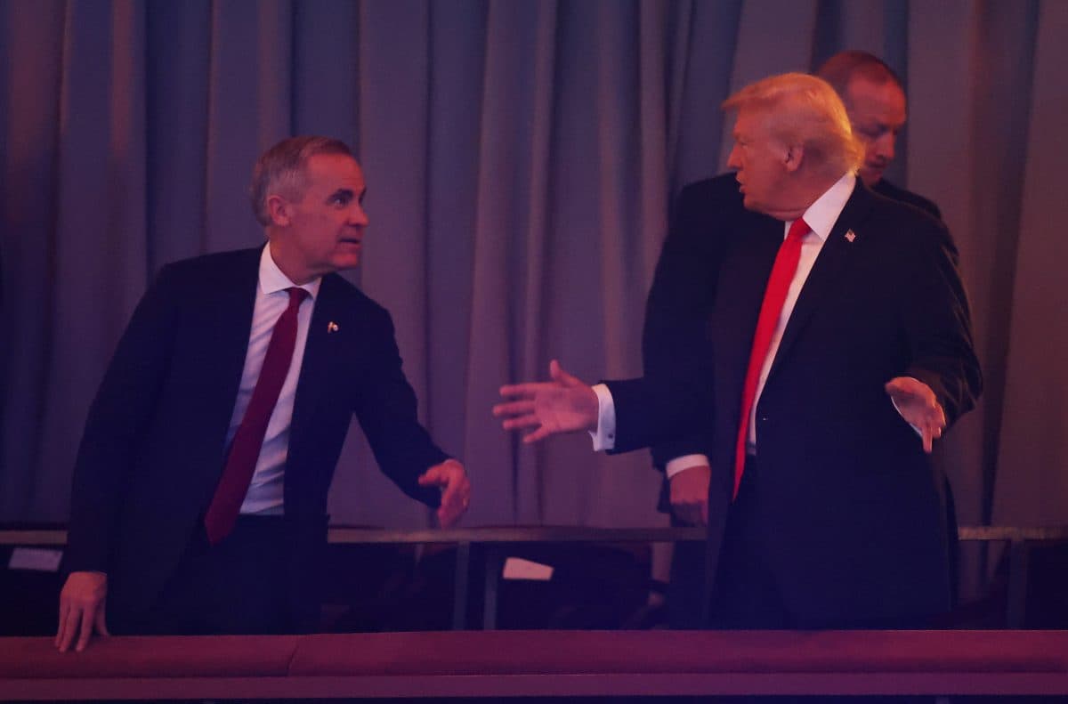 To menn i dress, den ene med rødt slips, ser ut til å hilse eller gestikulere til hverandre i et forhengt rom med en tredje mann i bakgrunnen.