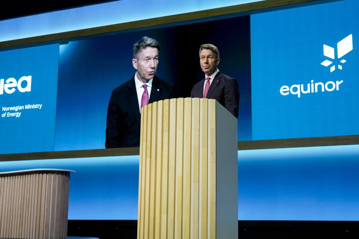 En mann i dress taler på et podium med en stor skjerm bak seg som viser bildet av ham sammen med logoene til IEA og Equinor.