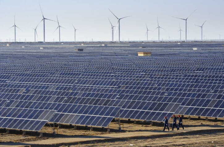 Workers walk past solar panels and wind turbines at a newly-built power plant in Hami