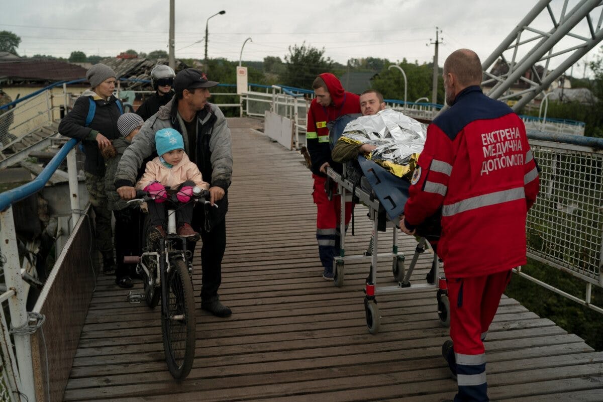 Såret soldat på båre; helsepersonell og sivile går over bro i Izium, Ukraina