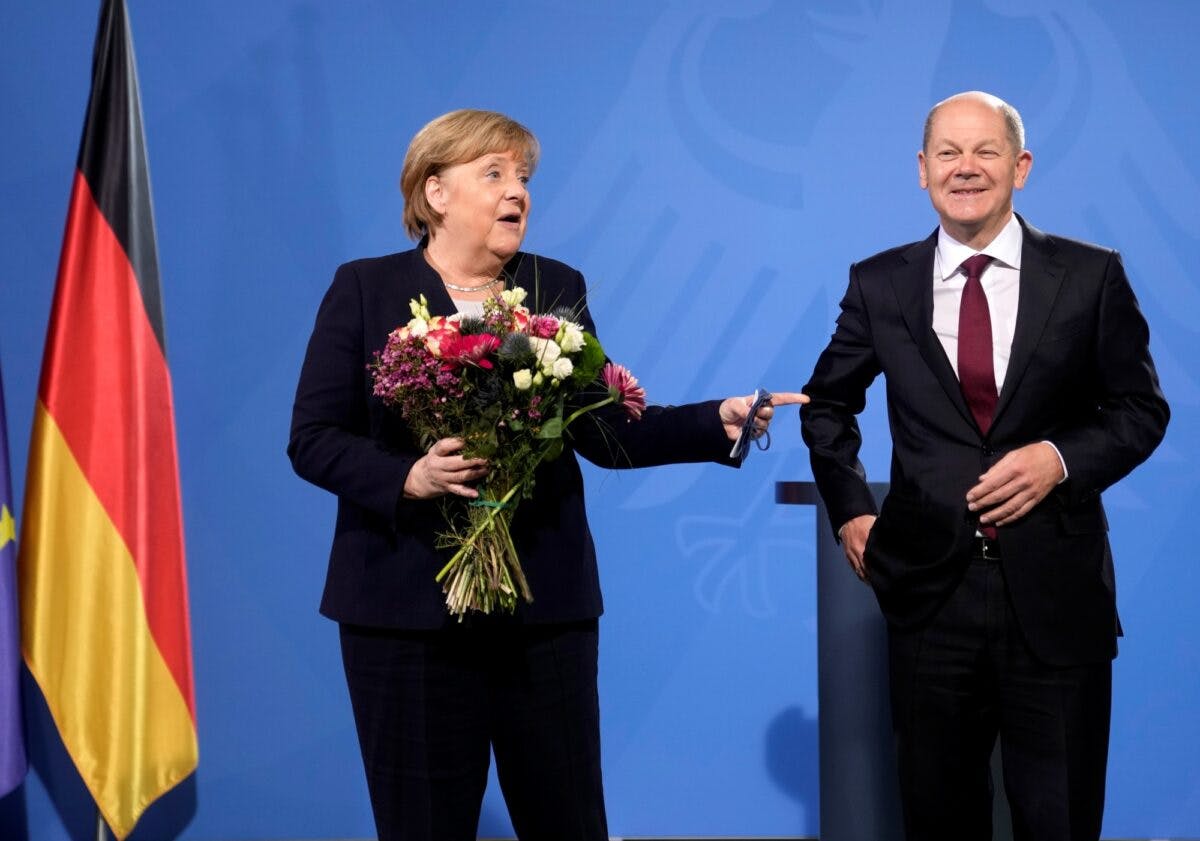 Merkel med blomsterbukett peker på Scholz