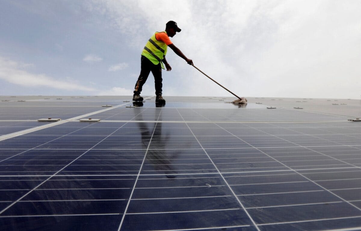 Mann rengjør solcellepaneler med kost.