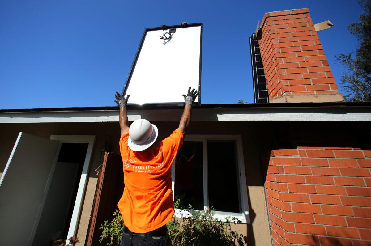 Mann rekker en solcellemodul opp mot et hustak