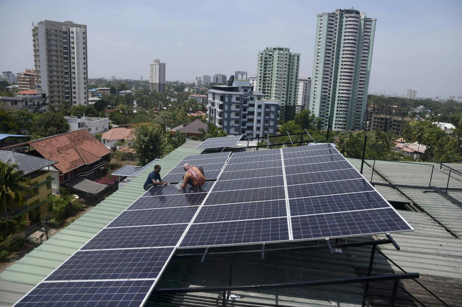 Arbeidere jobber med solceller på toppen av et bygg i en by