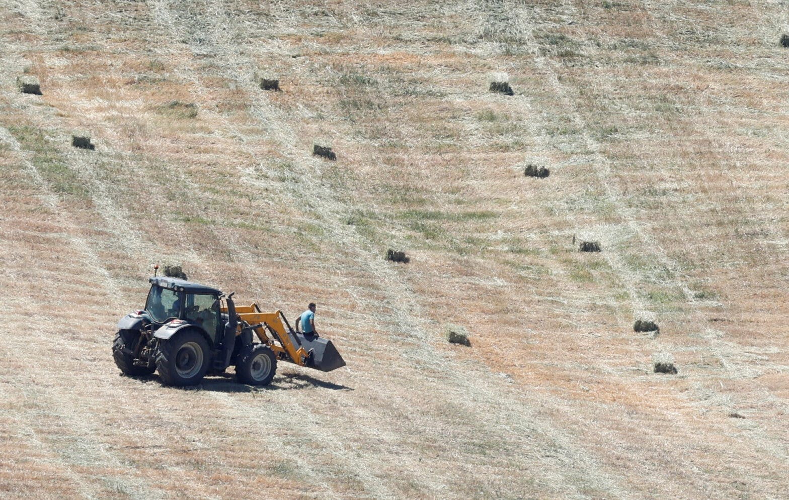 Traktor står på et tørt jorde med små høyballer