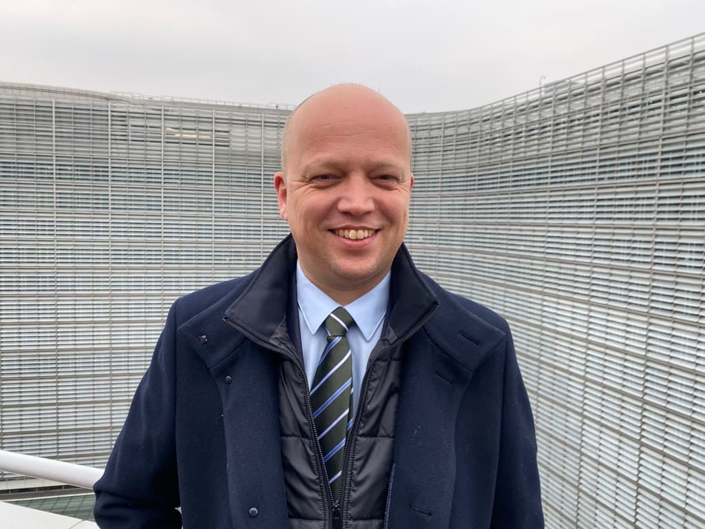 En skallet mann i dress og slips som står foran en bygning.