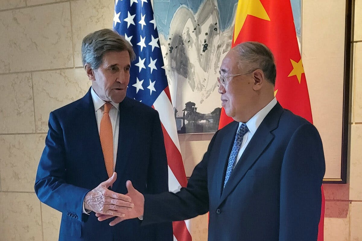 To menn i dress håndhilser foran et amerikansk og kinesisk flagg.