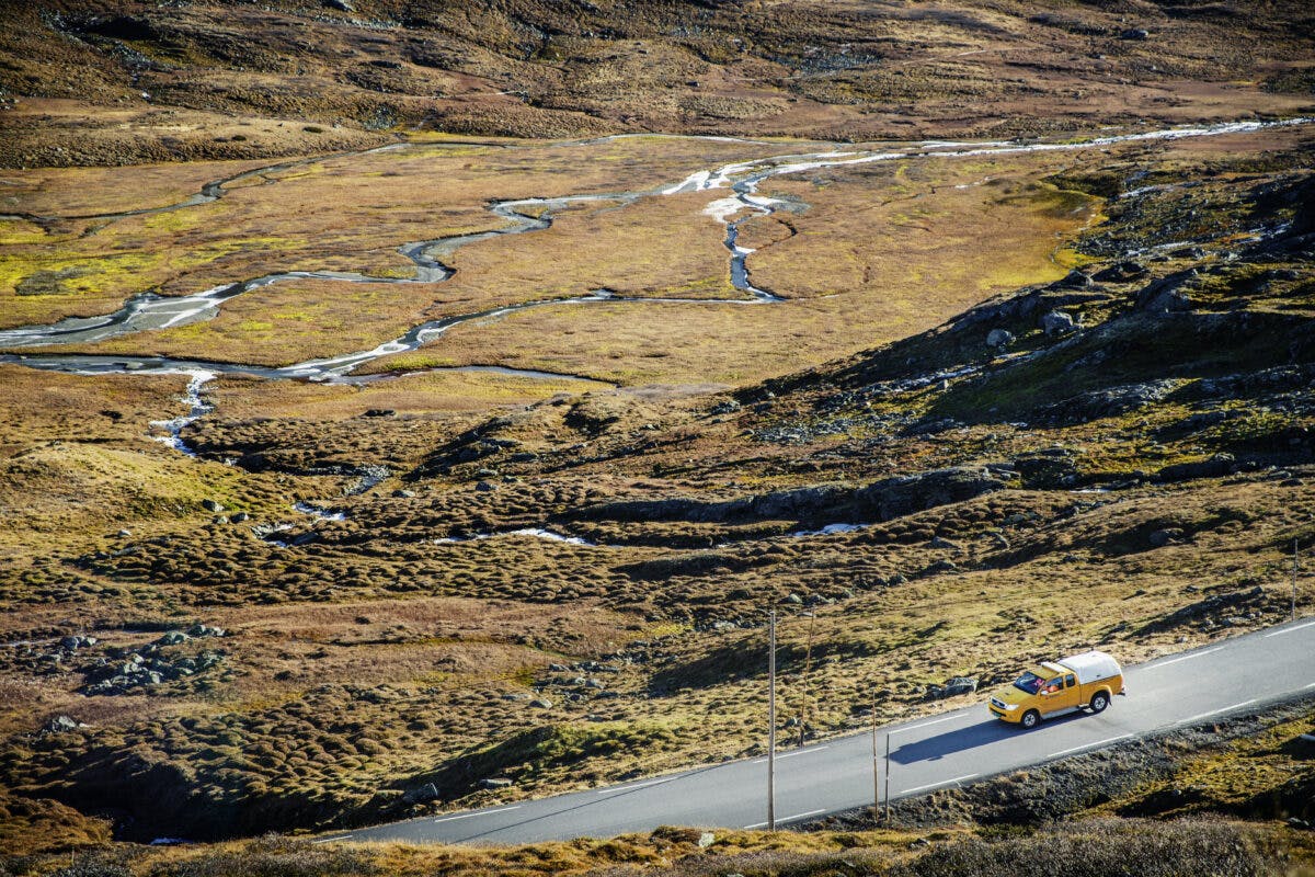 En gul lastebil kjører nedover en vei nær en elv.