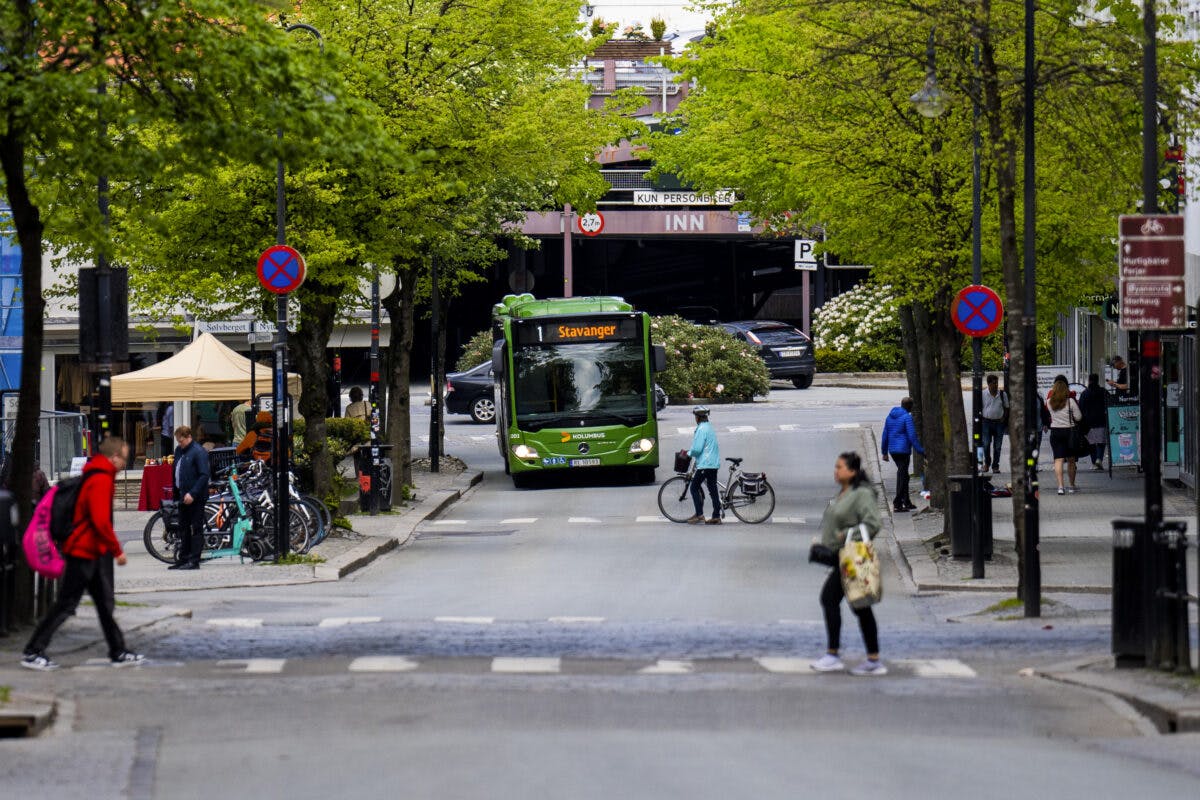 En grønn buss kjører nedover en bygate.