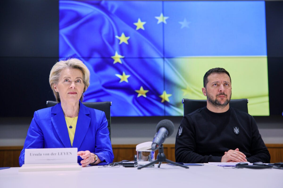 To personer sitter ved et bord foran et ukrainsk flagg.