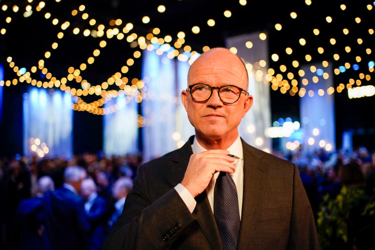 En skallet mann i dress og slips som står foran en folkemengde.