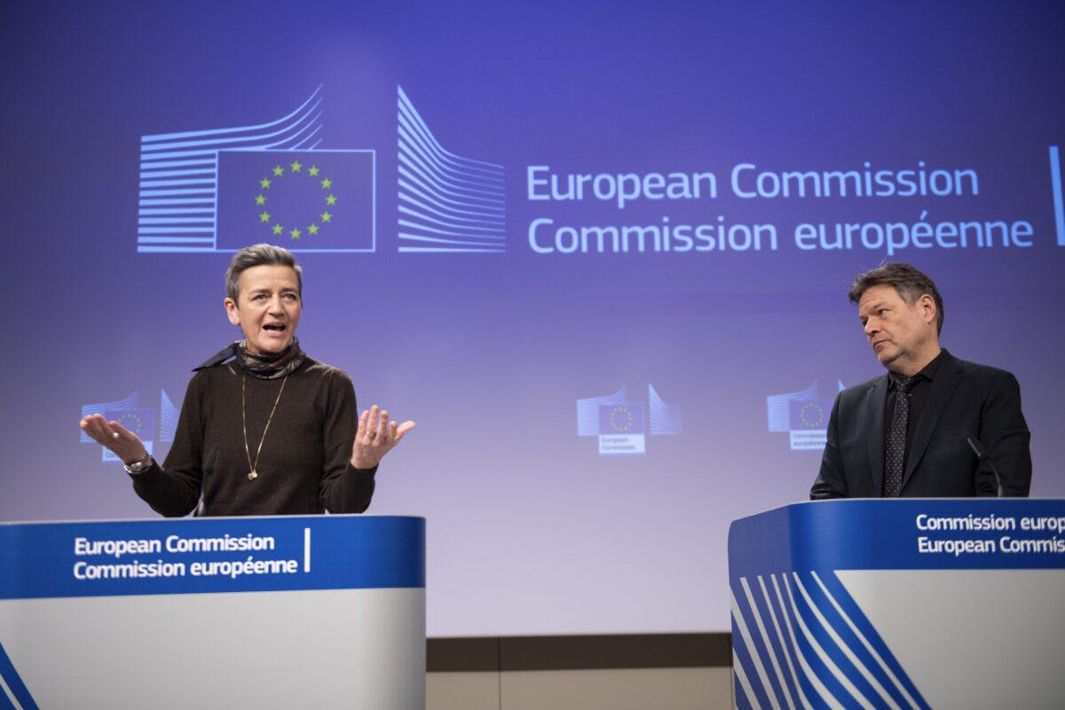 To personer står ved podier foran et skilt fra Europakommisjonen.