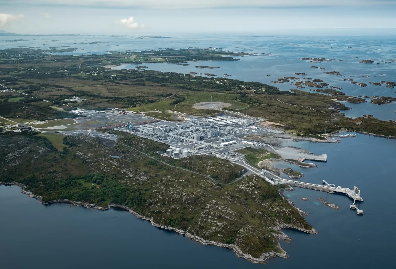 Luftfoto av et industrianlegg som ligger i et steinete kystlandskap omgitt av vann og små øyer.