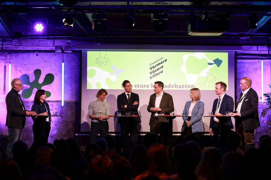 Politikerpanel på scenen med Varmere Våtere Villere logo i bakgrunnen og publikum i forgrunnen