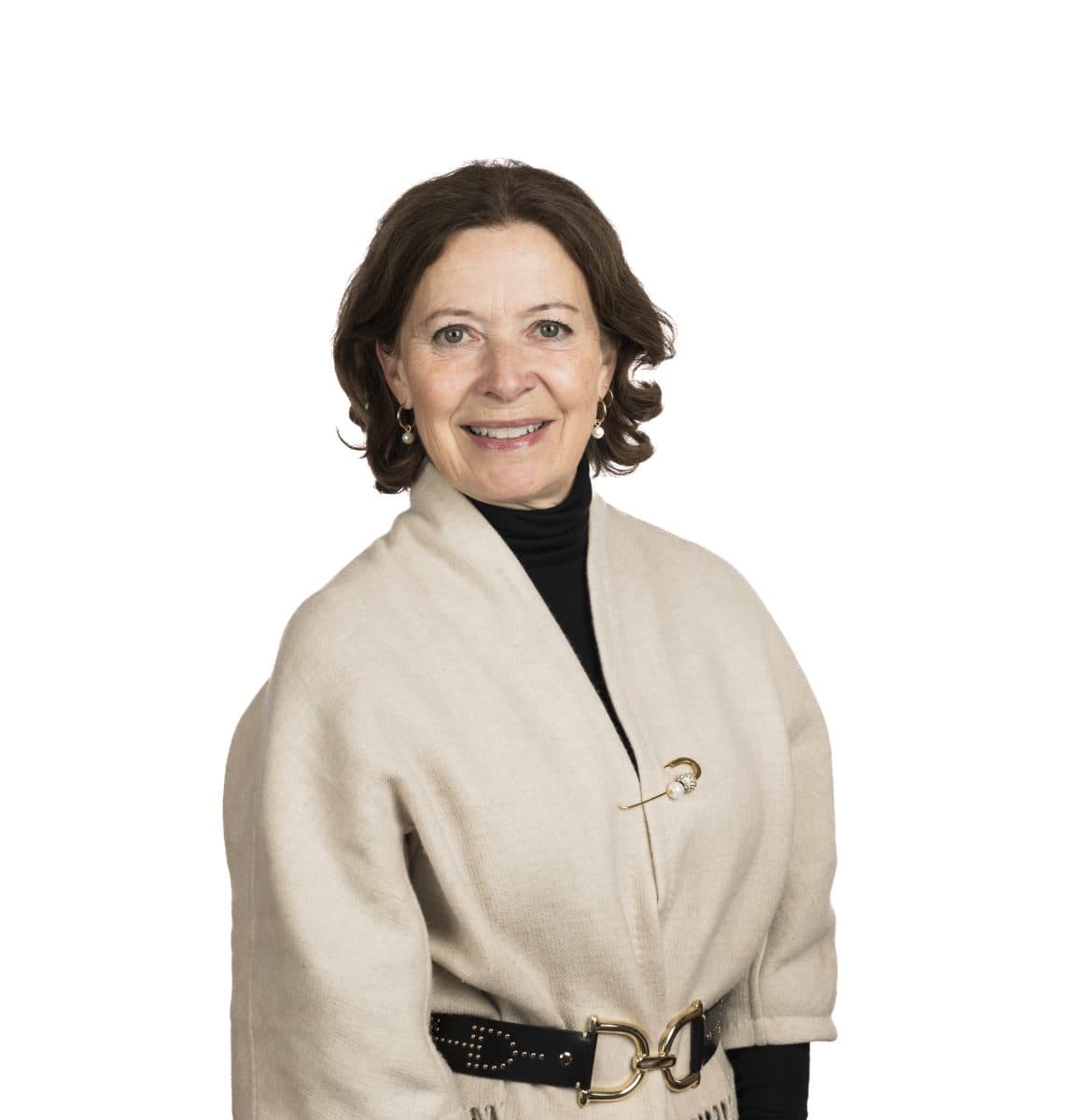 En kvinne med skulderlangt, brunt hår, iført beige slå-om-frakk med svart rullekrage og belte, smiler til kameraet mot en enkel, hvit bakgrunn.