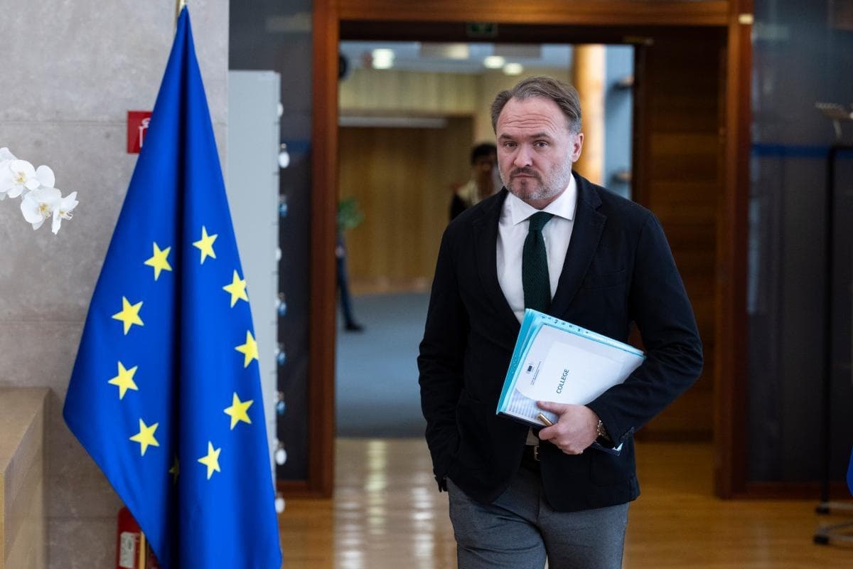 En mann i dress med dokumenter i hånden går forbi et EU-flagg inne i en kontorbygning.