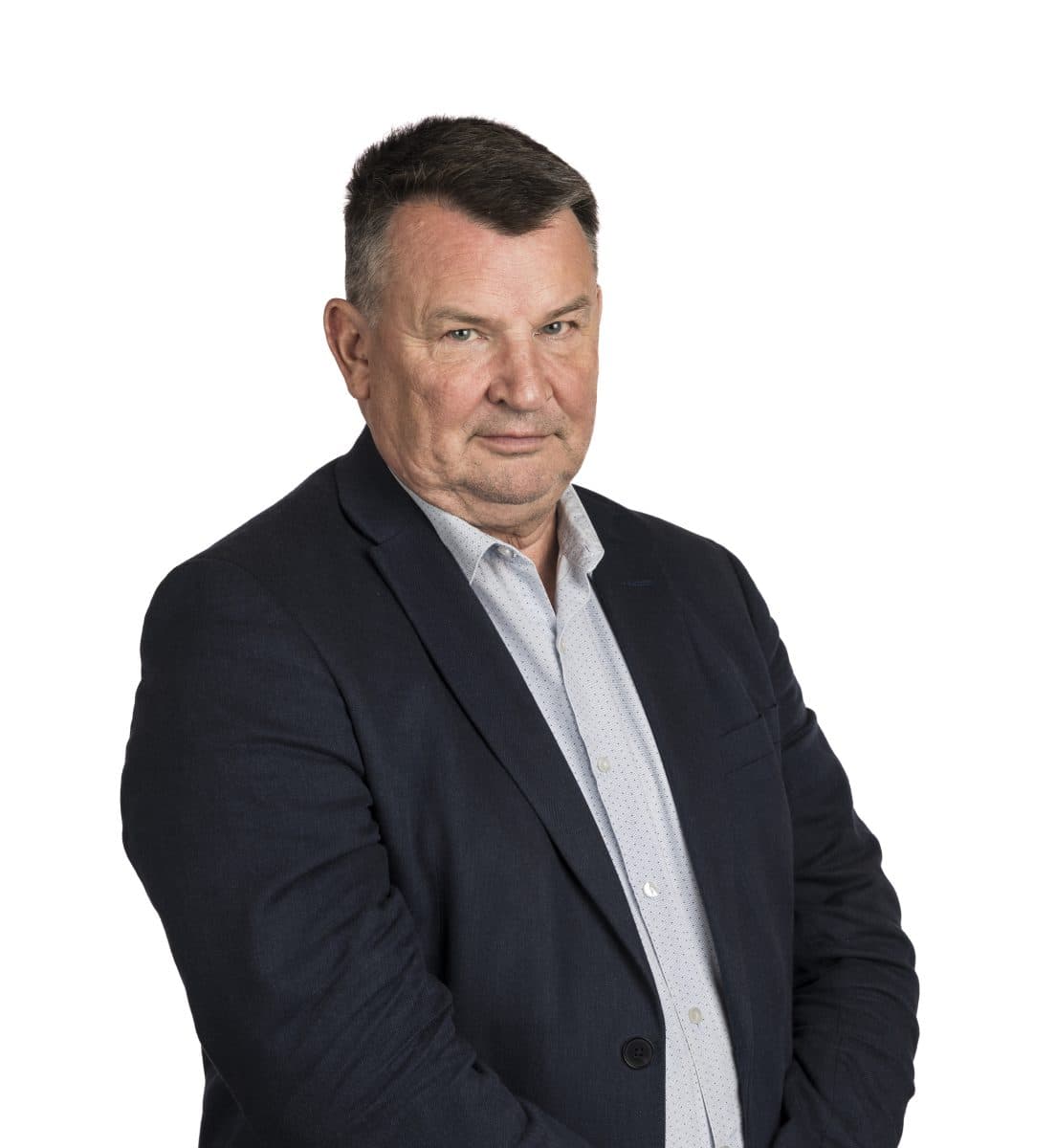 En middelaldrende mann med kort, mørkt hår, iført marineblå blazer og lys skjorte, står mot en enkel, hvit bakgrunn.