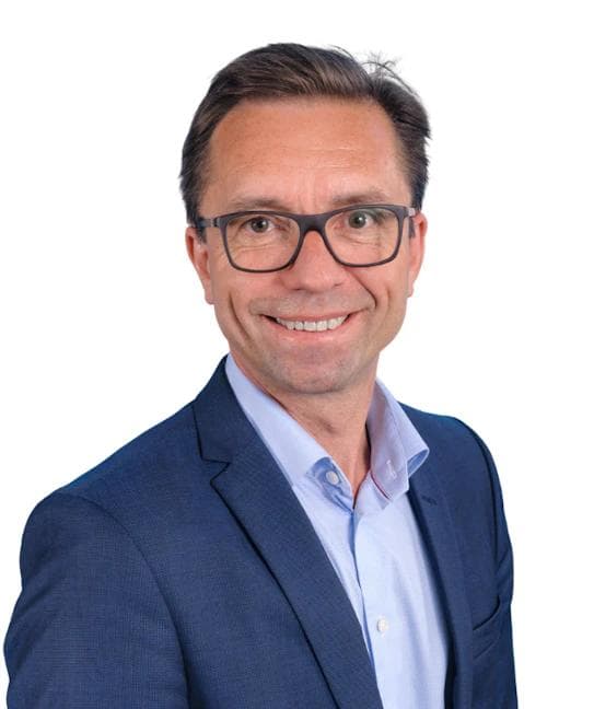 Smilende mann med briller i blå dress og lyseblå skjorte.