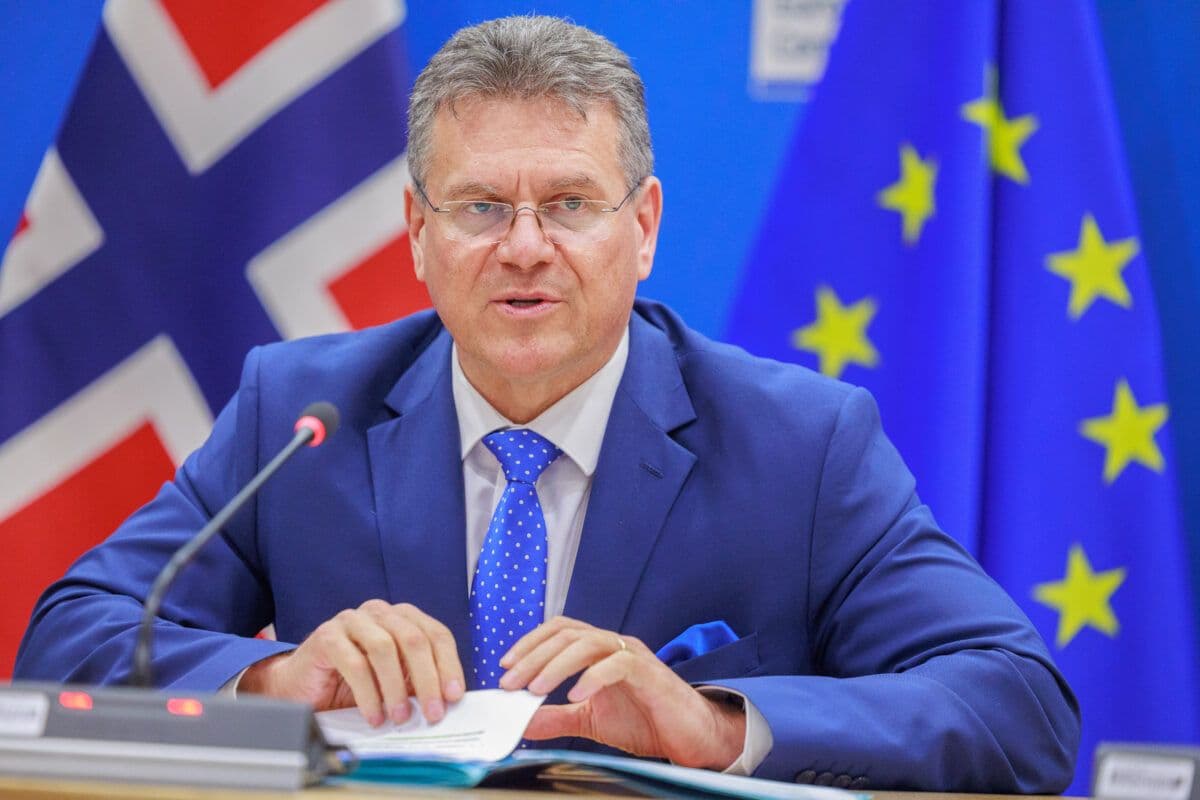 Mann i blå dress som sitter foran flaggene i Storbritannia og EU under et møte.