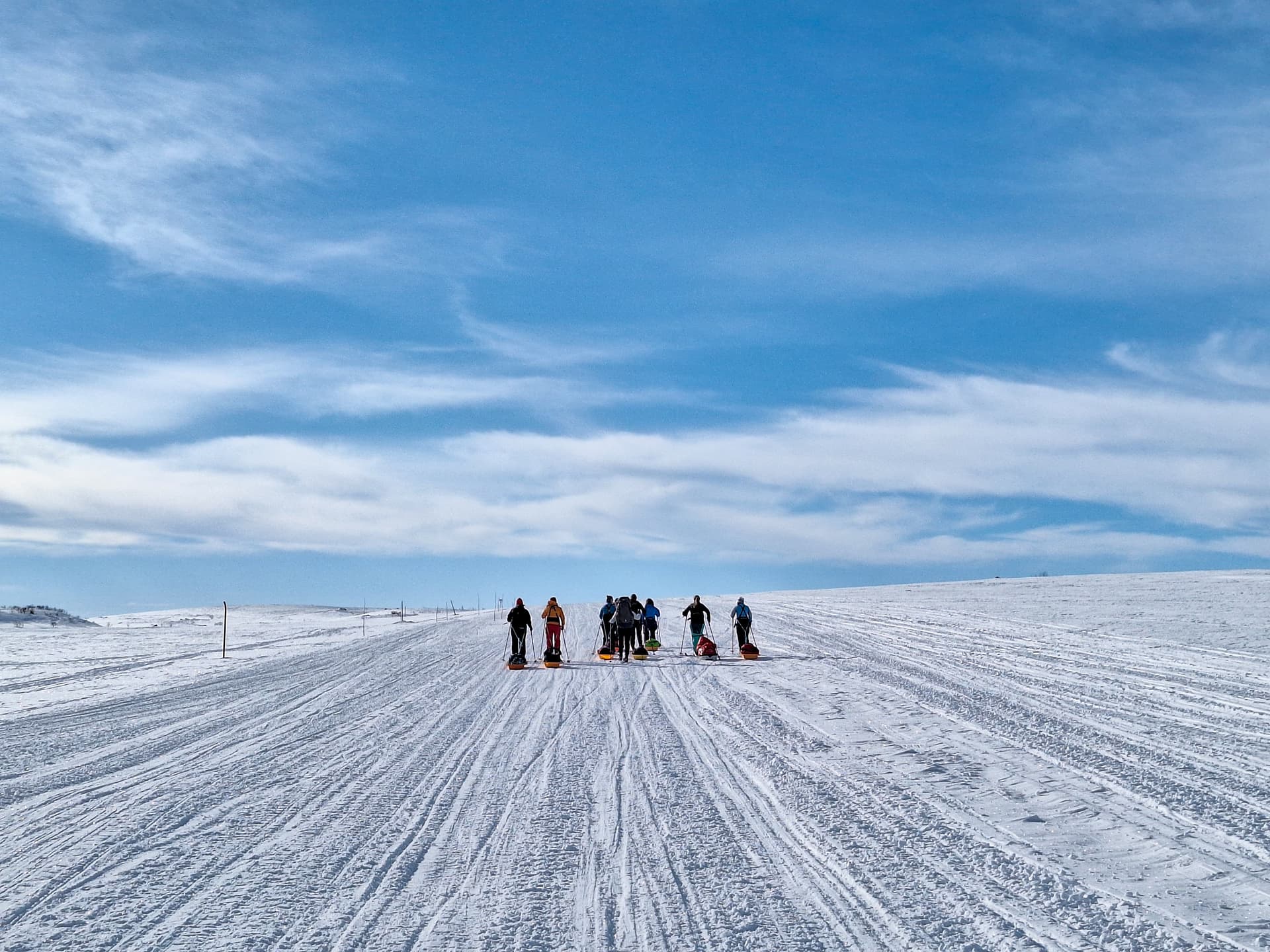 En gruppe mennesker som trekker sleder over et enormt, snødekt landskap under en blå himmel.