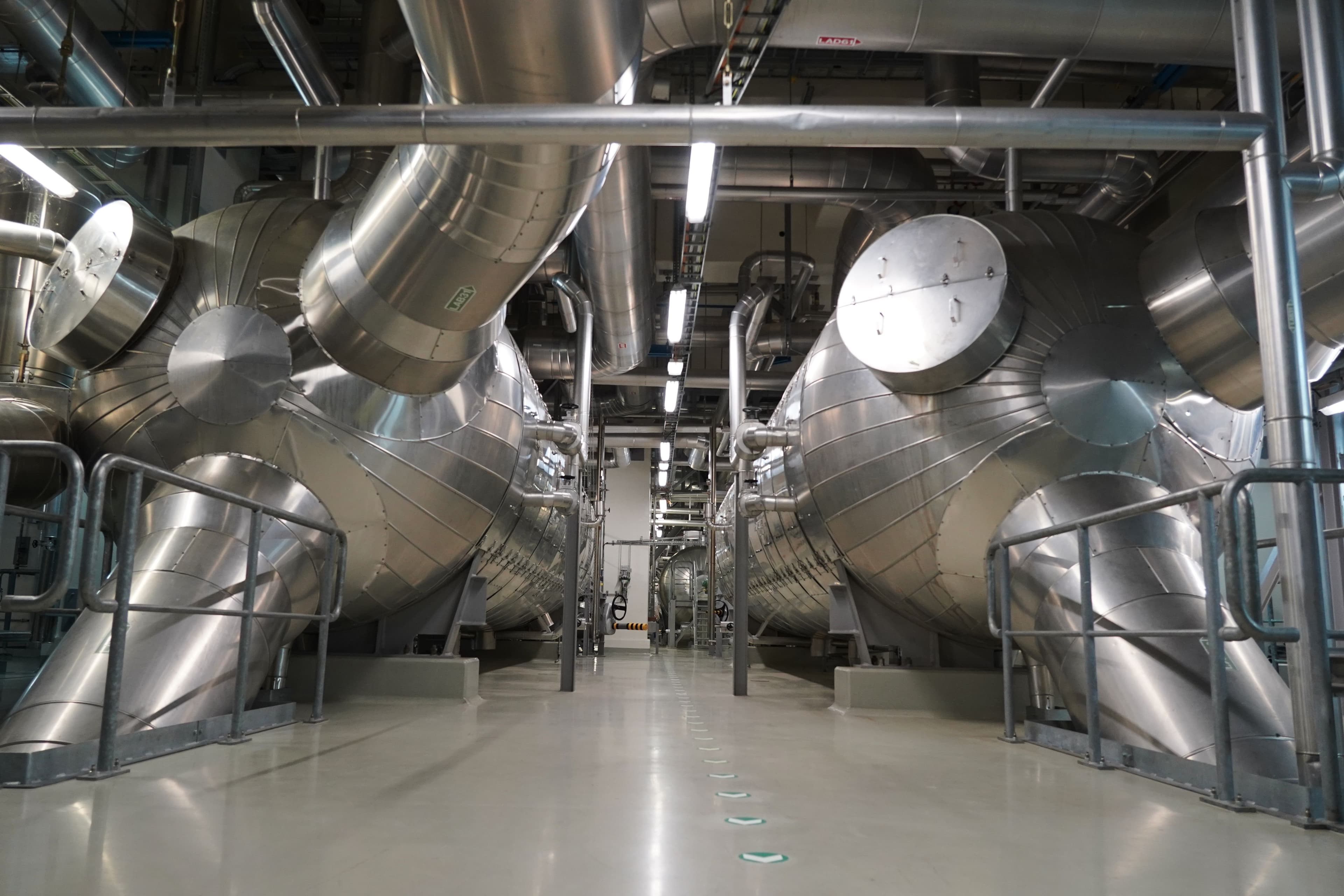 Et rent industrianlegg med to rekker av store, isolerte sølvfargede maskiner og et omfattende rørsystem i taket.