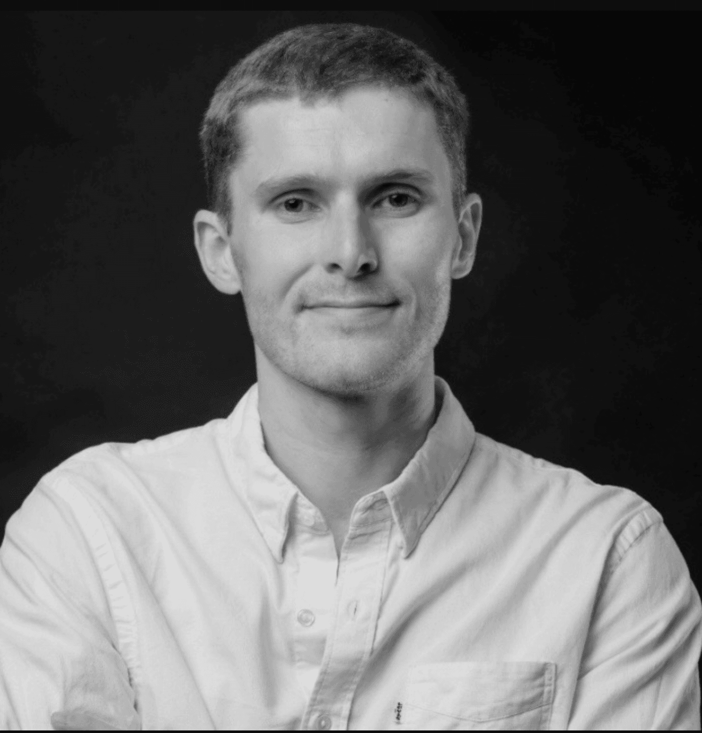 Svart-hvitt-portrett av en smilende mann i skjorte med krage.