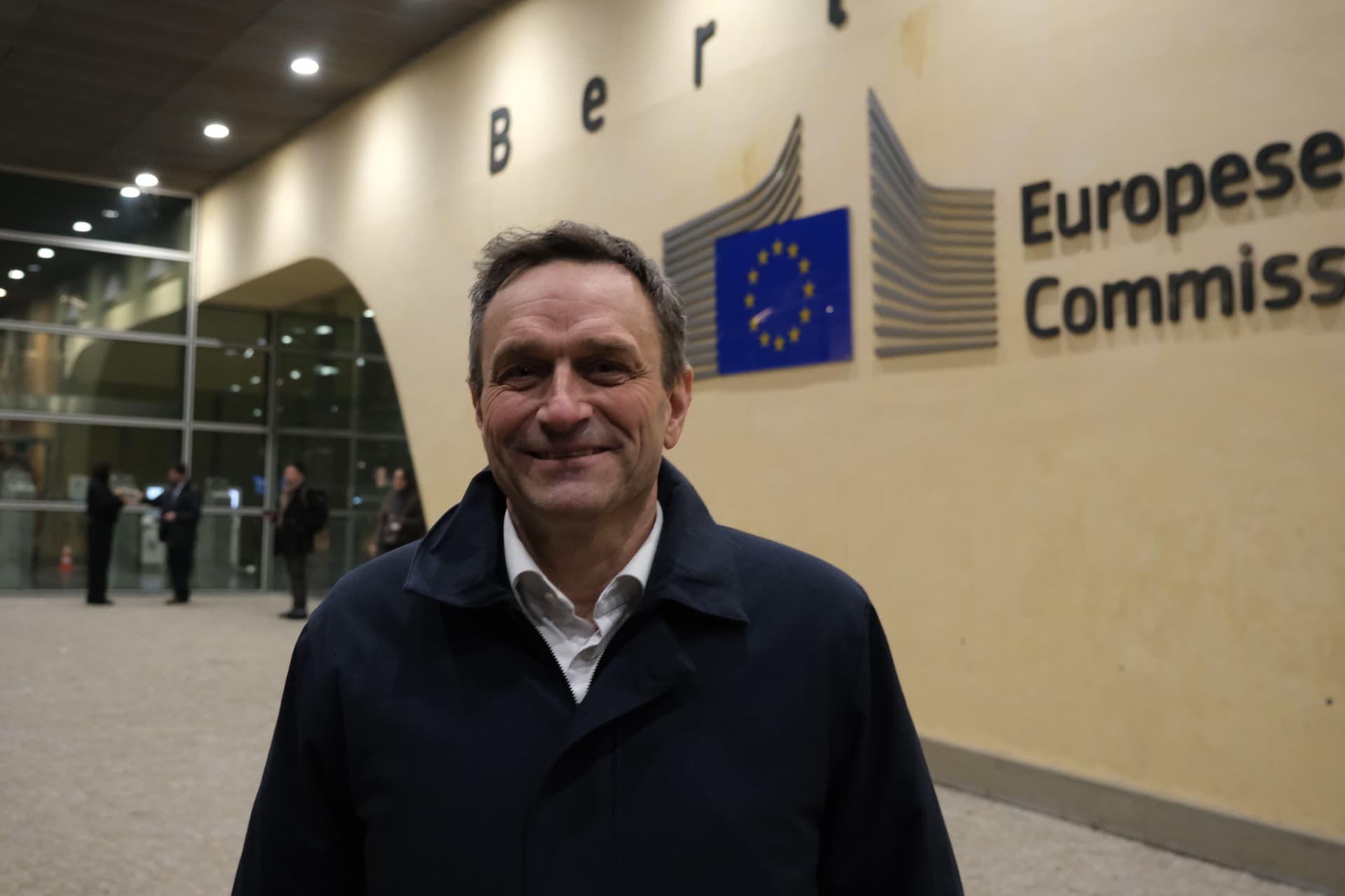 En smilende mann står foran et skilt for Europakommisjonen.