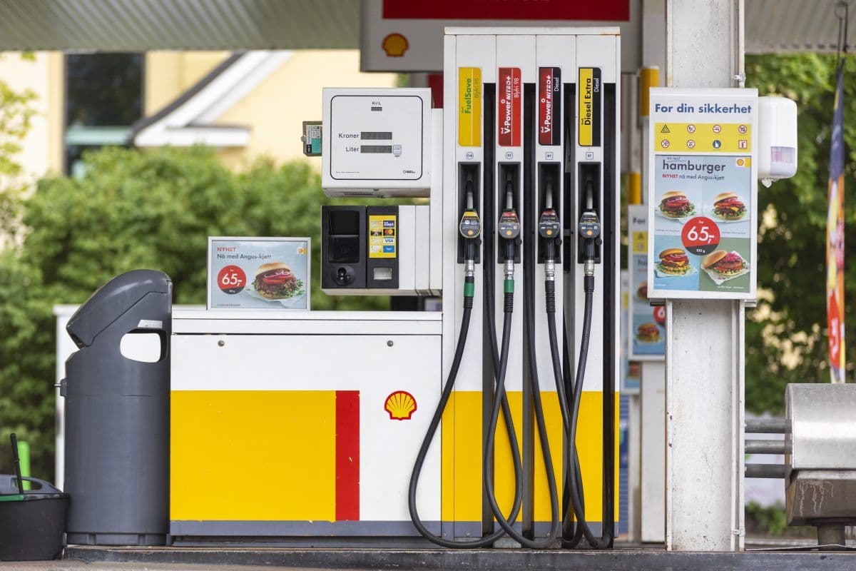En Shell-bensinstasjon med fire drivstoffautomater, en betalingsterminal, en søppelbøtte og et reklameskilt som reklamerer for hamburgere til 65 valutaenheter.