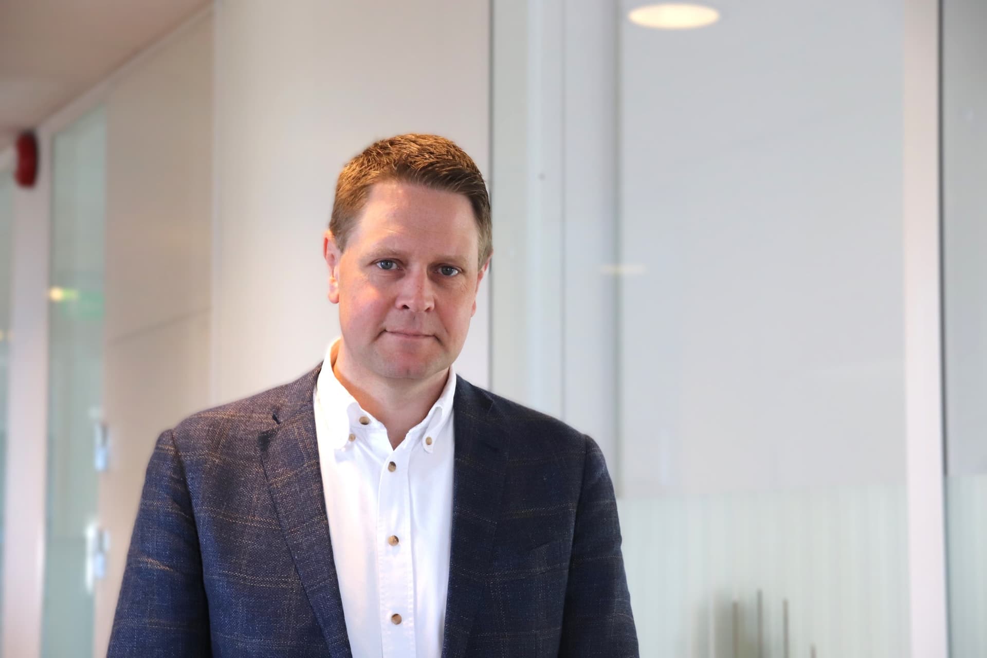 En mann i blå rutete dressjakke og hvit skjorte står på et kontor.