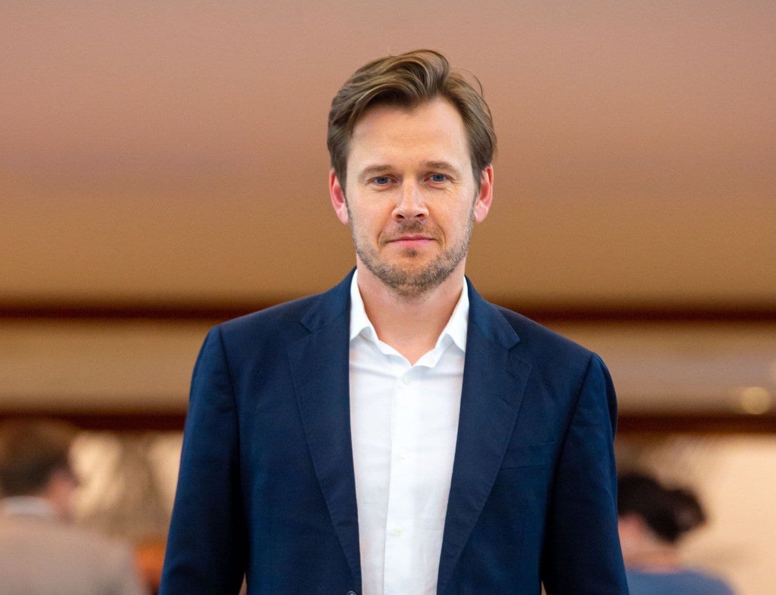 En mann i marineblå dress og hvit skjorte går fremover og ser mot kameraet.