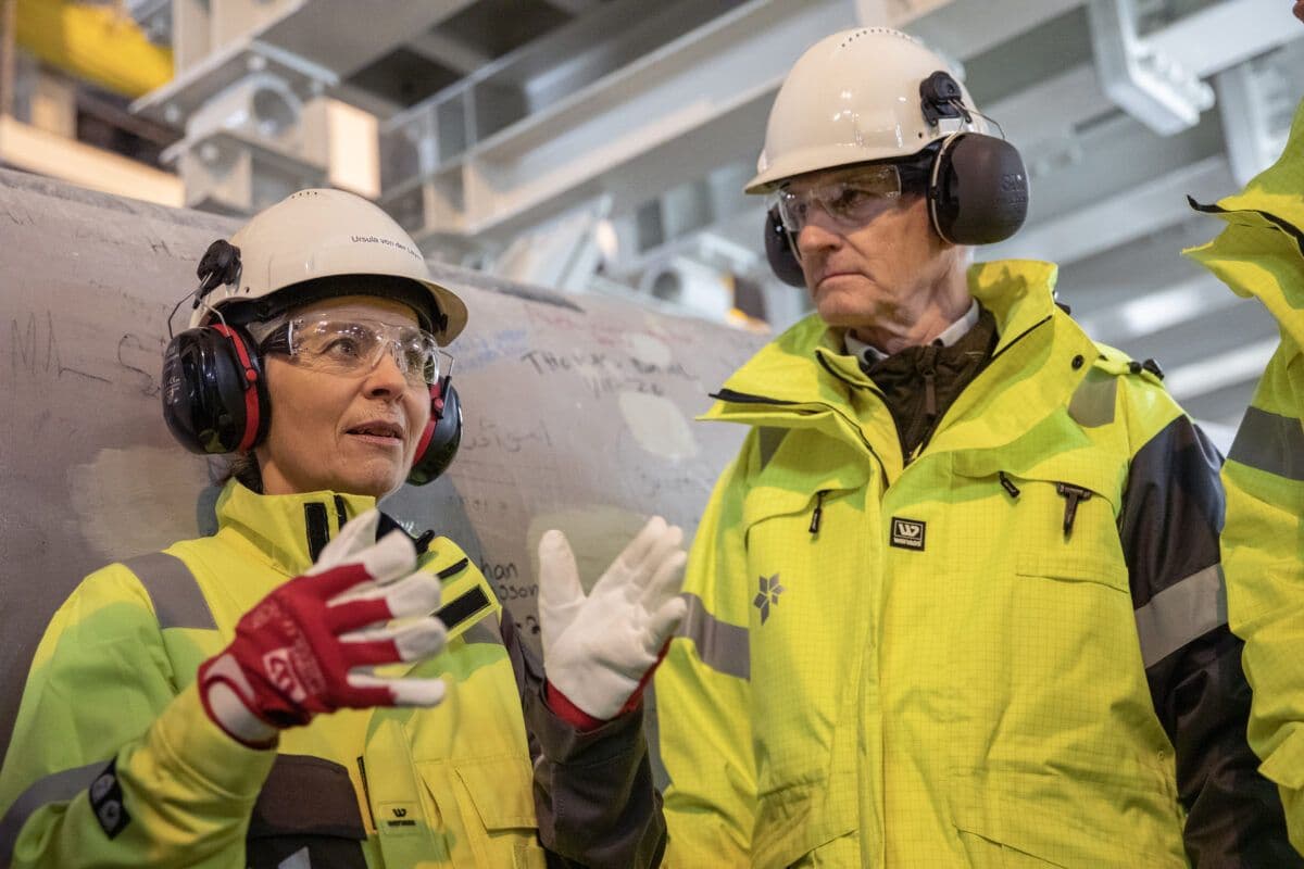 Tre personer i gule jakker snakker med hverandre.