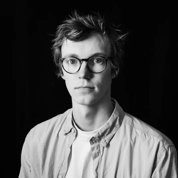 Et svart hvitt bilde av en ung mann med briller og kort hår