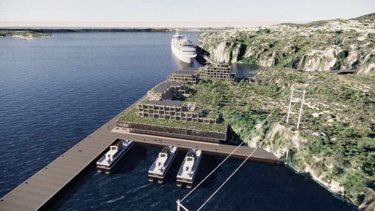 Flyfoto av et kystområde med moderne bygninger, en brygge med småbåter, et stort cruiseskip og omkringliggende grøntområder langs strandlinjen.