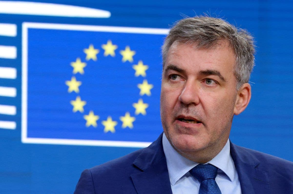 En mann i dress snakker foran en blå bakgrunn med EU-flagget med gule stjerner i en sirkel.